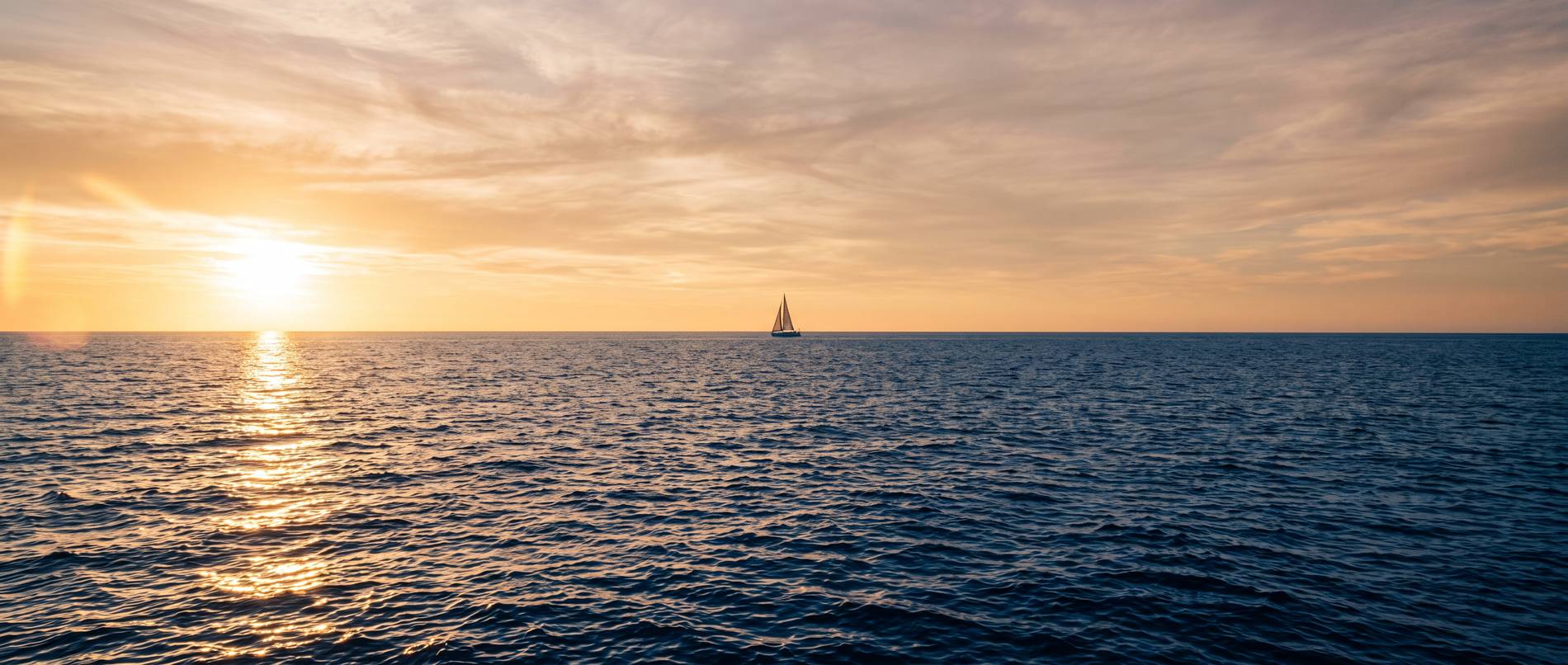 Velero en el horizonte al atardecer en mar abierto
